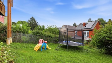 Un jardin avec un trampoline, un toboggan et une cabane en bois.