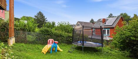 Un patio trasero con un trampolín, un tobogán y una casita de juegos de madera.