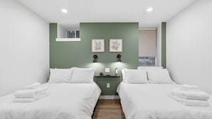 A hotel room with two beds, a small window, and a wall-mounted shelf with a clock.
