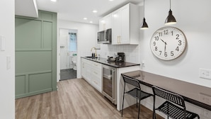 A modern kitchen with white cabinets, a black countertop, a stainless steel refrigerator, and a wall clock.