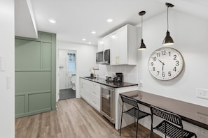 A modern kitchen with white cabinets, a black countertop, a stainless steel refrigerator, and a wall clock.