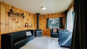 Ein Zimmer mit Holzeinrichtung, einem schwarzen Sofa, einem blauen Sessel, einem Kamin und einem mit Vorhängen drapierten Fenster.