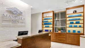 Un área de recepción con un mostrador de madera, un letrero en la pared que dice 'MANDARA SPA' y estanterías con cajas azules.