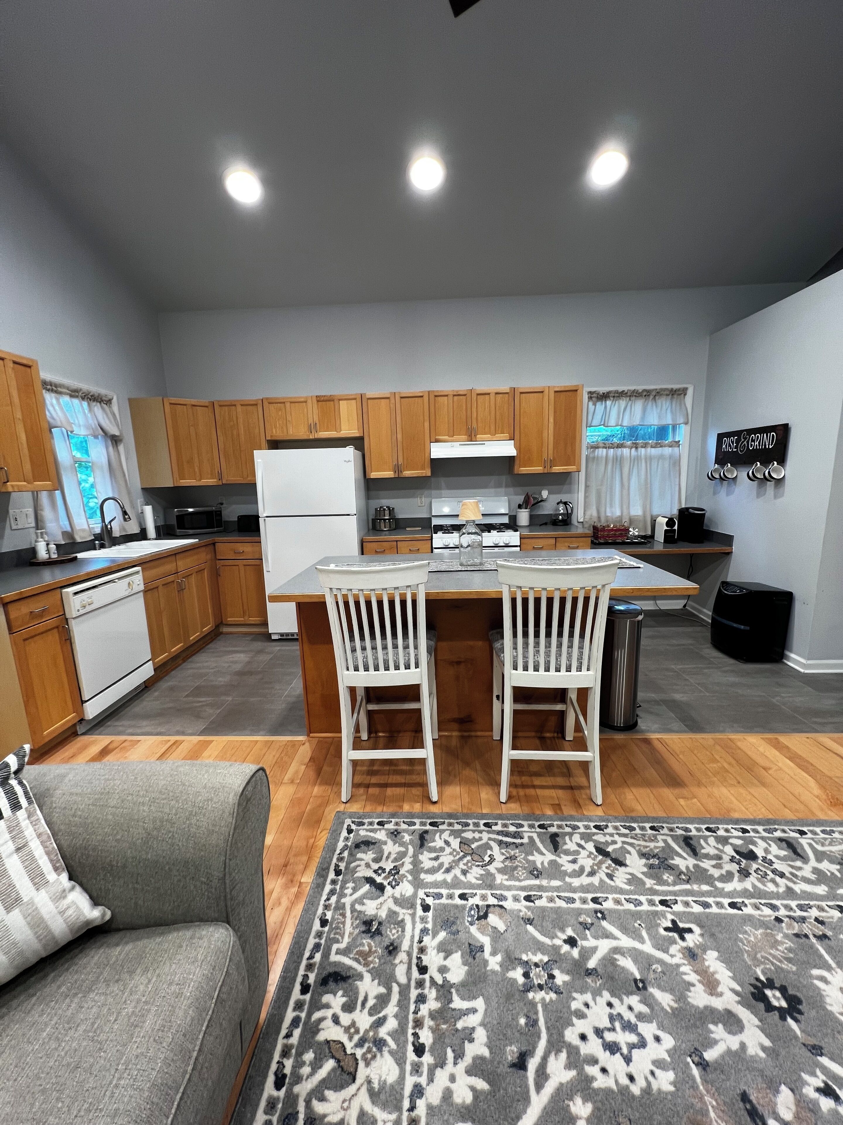 Une cuisine moderne avec des meubles en bois, un îlot central doté de chaises, un réfrigérateur, un four à micro-ondes et une cuisinière.