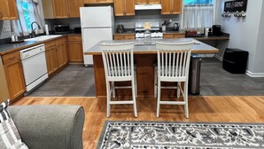A modern kitchen with wooden cabinets, a central island with chairs, a refrigerator, microwave, and a stove.