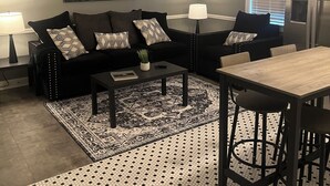 A modern living room with a black sofa, a coffee table, a dining table, and a ceiling fan. - Comfort and Style, Modern Corporate Apartment in Pascagoula (Pascagoula)