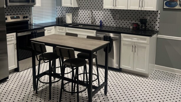 A modern kitchen with white cabinets, a black countertop, a dining table with four chairs, and a tiled floor. - Comfort and Style, Modern Corporate Apartment in Pascagoula (Pascagoula)