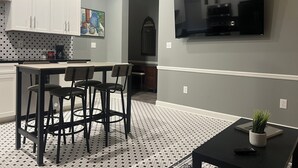 A modern kitchen with white cabinets, a dining area with a table and chairs, a TV mounted on the wall, and a patterned floor. - Comfort and Style, Modern Corporate Apartment in Pascagoula (Pascagoula)