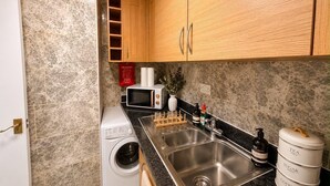Een keuken met een wasmachine, magnetron, spoelbak en kastjes.