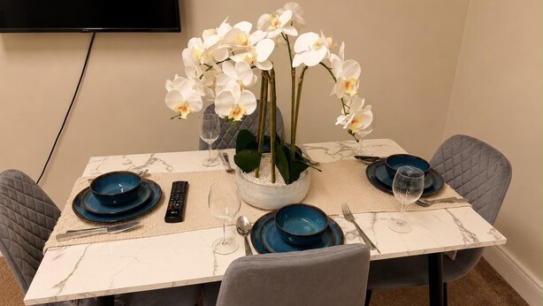 Een eettafel met blauwe borden, een afstandsbediening en een vaas witte bloemen.