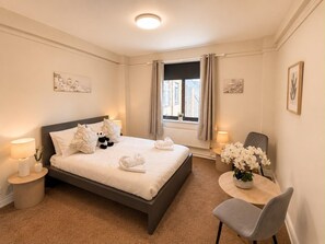 Ein Hotelzimmer mit Bett, einem runden Tisch mit Stuhl, einem Fenster mit Vorhängen und Wandbildern.