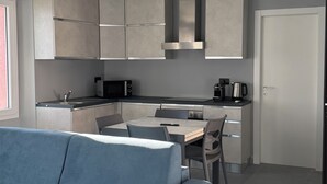 Eine moderne Küche mit grauen Schränken, ein Essbereich mit einem blauen Sofa und ein Fliesenboden.