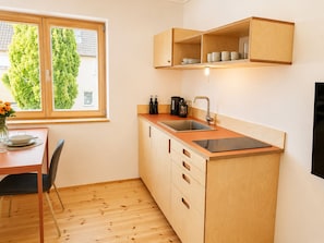 A compact kitchen with a built-in sink, wooden cabinets, and a window with a view of trees.