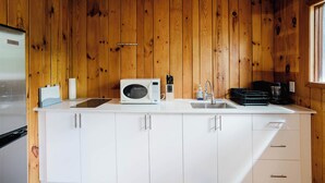 A kitchen with wooden walls, white cabinets, a microwave, a sink, and a coffee maker. - 3 Bedroom Cottage V: SB (Carling)