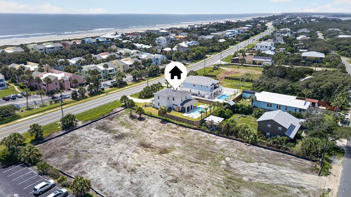 Vue aérienne d’un quartier résidentiel avec des maisons, une route et une plage en arrière-plan.