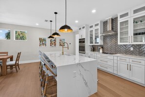 A modern kitchen with white cabinets, a marble island, pendant lighting, and a herringbone-patterned backsplash. - Luxury Beach Retreat I Heated Saltwater Pool (Saint Augustine)