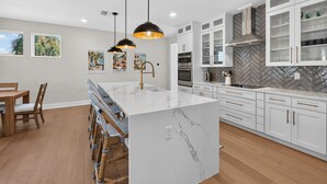 Una cocina moderna con armarios blancos, una isla de mármol, iluminación colgante y un salpicadero con motivo de espiga.