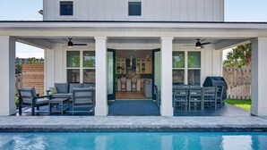 Una casa moderna con piscina, mobiliario de exterior y un patio cubierto.