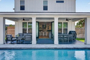 Ein modernes Haus mit Pool, Sitzgelegenheiten im Freien und einer überdachten Terrasse.