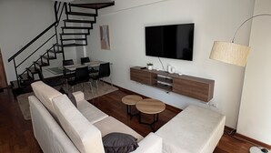 Ein modernes Wohnzimmer mit Treppe, Flachbildfernseher, Essbereich und einer Sofagarnitur.