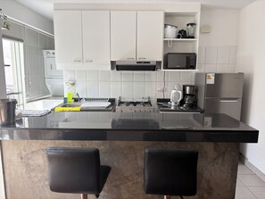 A modern kitchen with white cabinets, a black countertop, a stove, a microwave, and a refrigerator. - Spacious Duplex in Miraflores 2 room (Miraflores)
