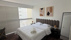 Ein modernes Schlafzimmer mit einem großen Bett, einem Nachttisch, einer Fensterbank und einem Fenster mit Jalousien.