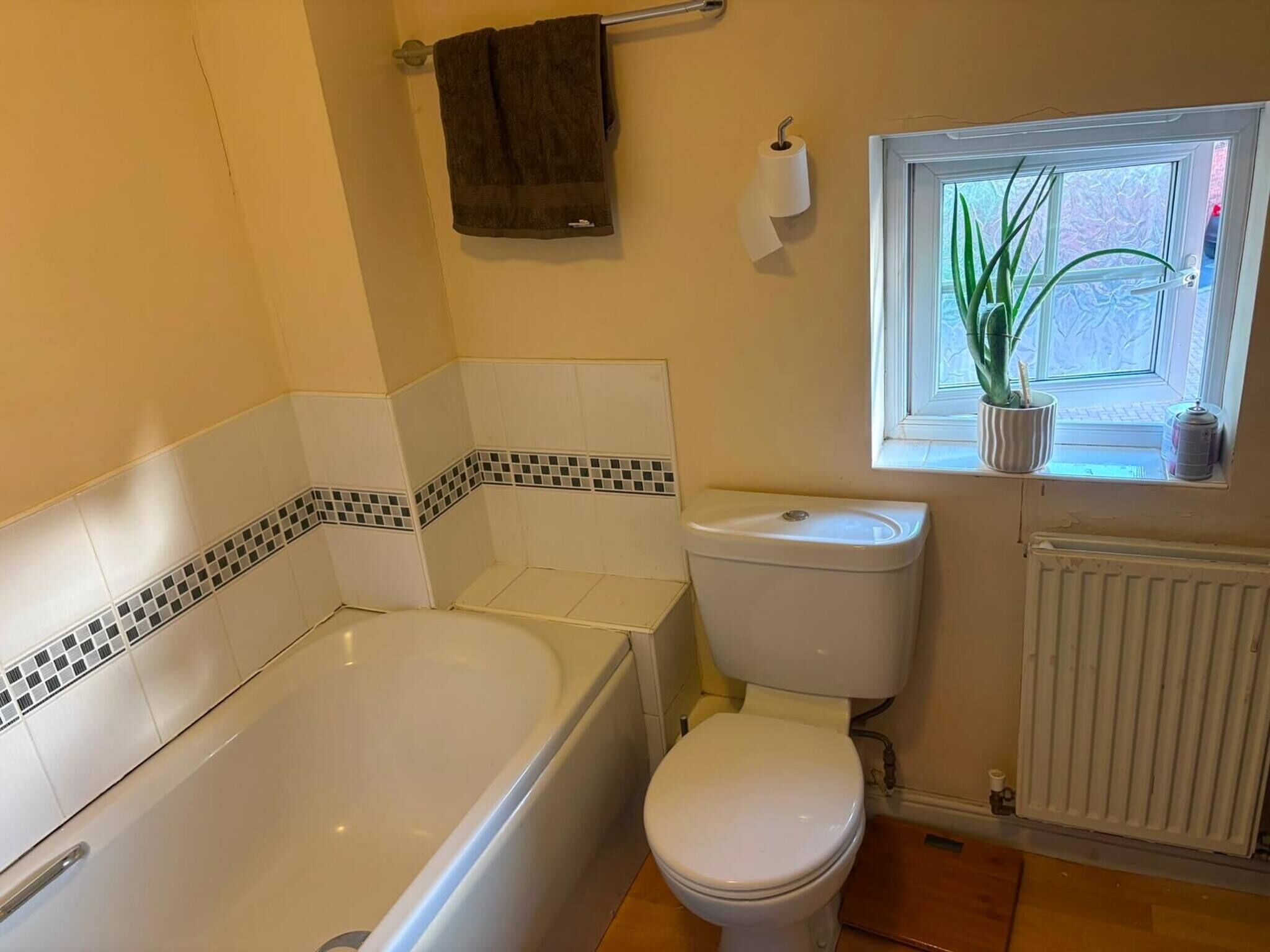 Et badeværelse med badekar, toilet og et vindue med en plante.