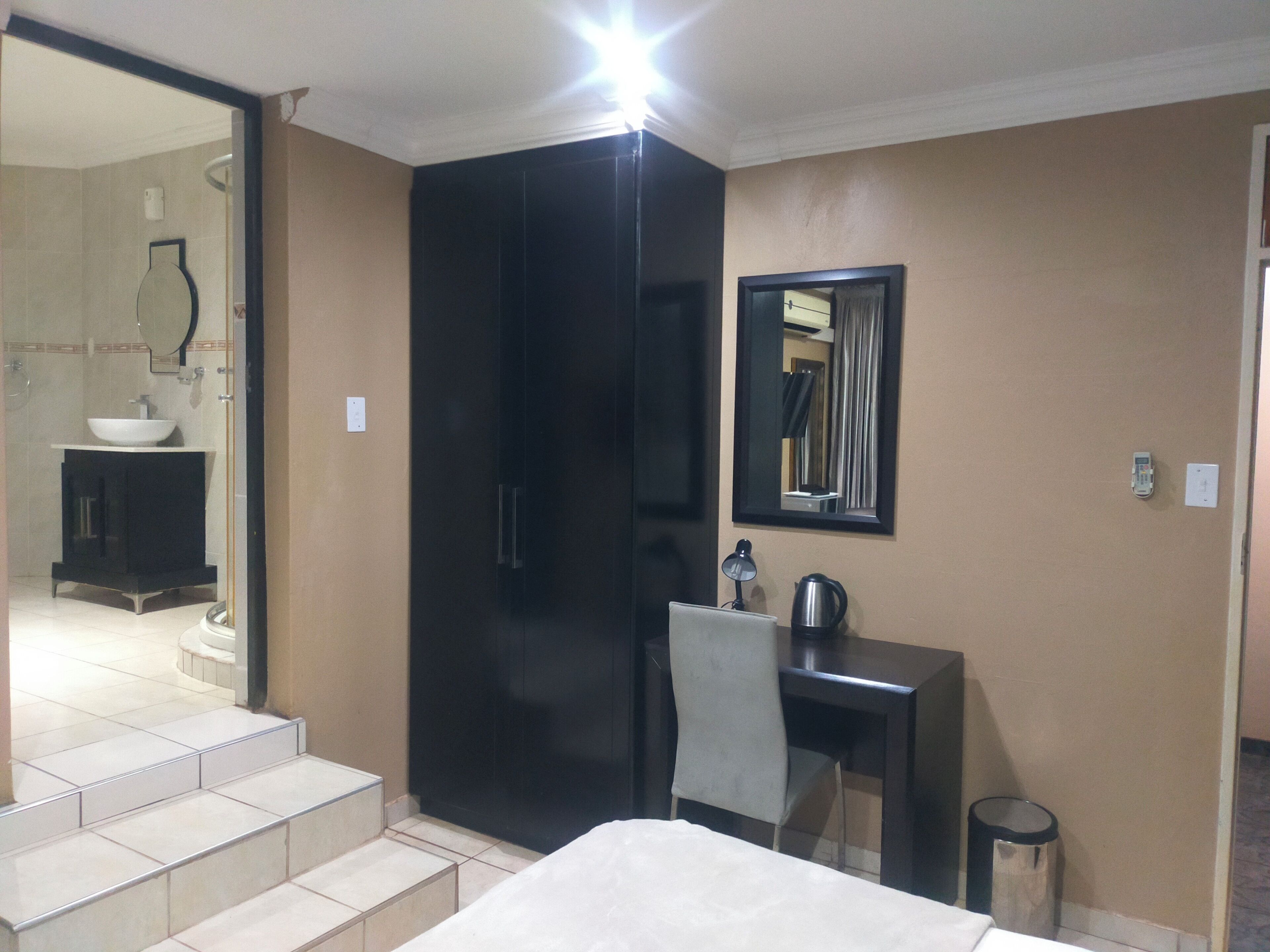A hotel room with a bed, a desk, a chair, a mirror, a sink, and a shower area.