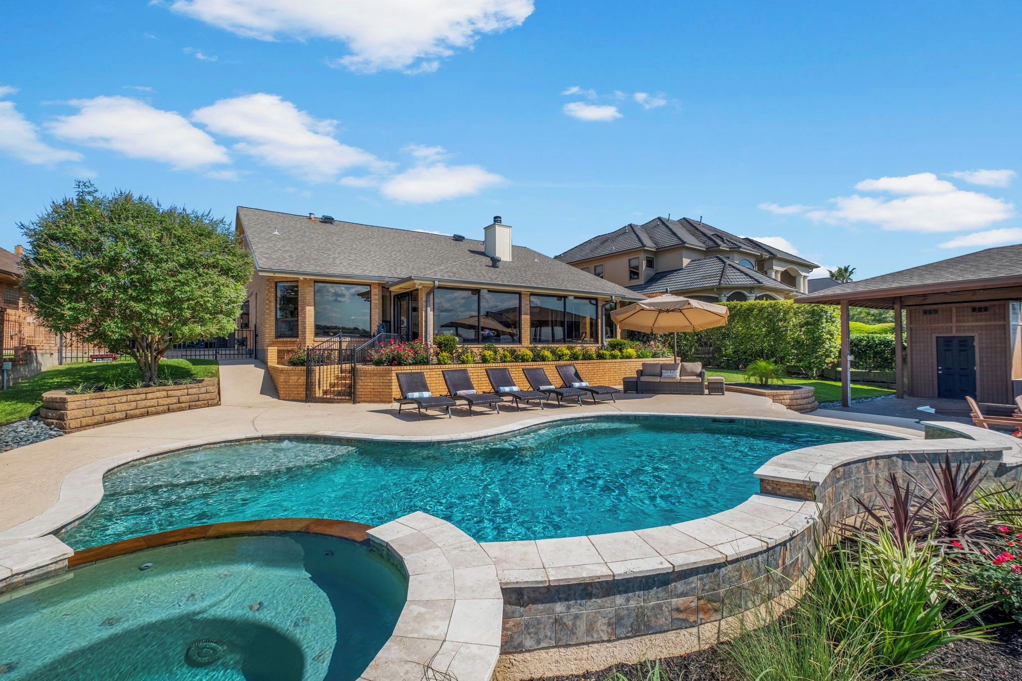 A residential property with a swimming pool, a covered patio with lounge chairs, and a landscaped garden.