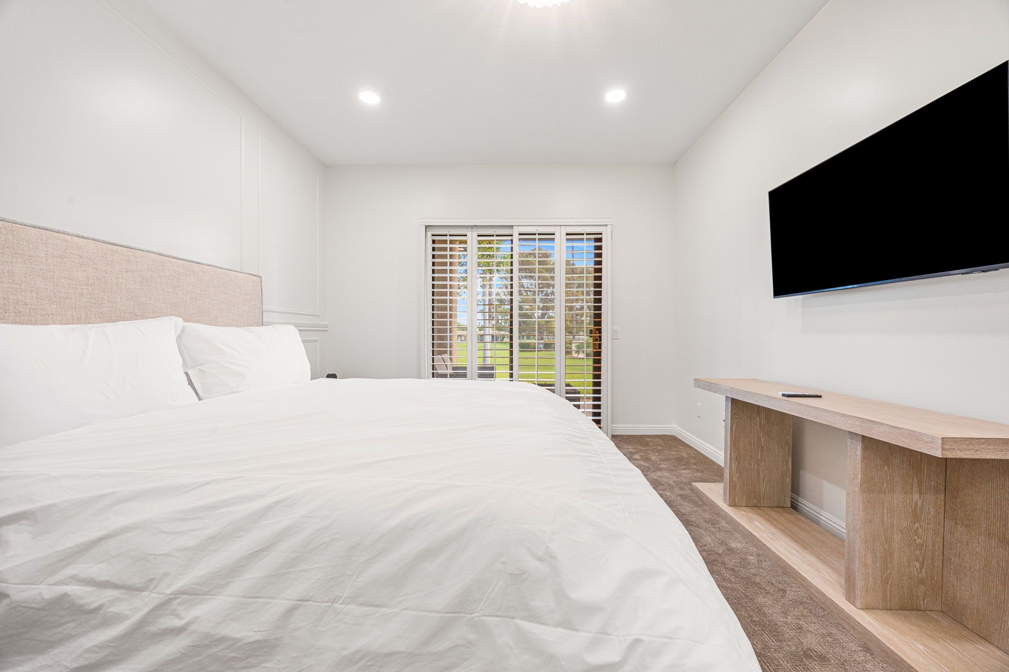 A modern hotel room with a large bed, a flat-screen TV mounted on the wall, and a sliding glass door leading to a balcony.