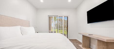 Et moderne hotelværelse med en stor seng, et fladskærms TV ophængt på væggen og en skydedør med glas til en balkon.