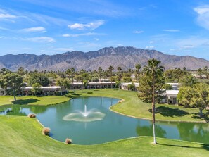 A golf course with a pond, palm trees, and mountains in the background. - Your Perfect Desert Retreat -Relax and Recharge in a fully remodeled 2 bed condo (Palm Springs)