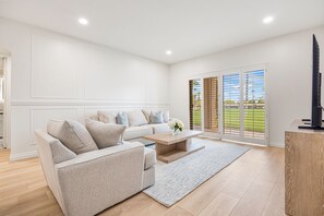 Ein modernes Wohnzimmer mit einer Eckcouch, einem Couchtisch und Blick durch große Schiebetüren auf einen Balkon.