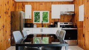 Une cuisine moderne avec des murs en bois, des armoires blanches, une table à manger avec des chaises et une vue sur la verdure à l’extérieur.
