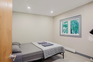 Een slaapkamer met een bed, een raam met uitzicht op bomen en een radiator.