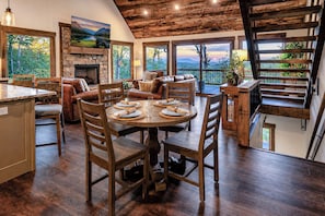 A spacious dining area with a round table, wooden chairs, and a stone fireplace. - Luxury Blue Ridge Cabin Layered Mountain View• Hot Tub • Sauna • Fire Pit (Blue Ridge)
