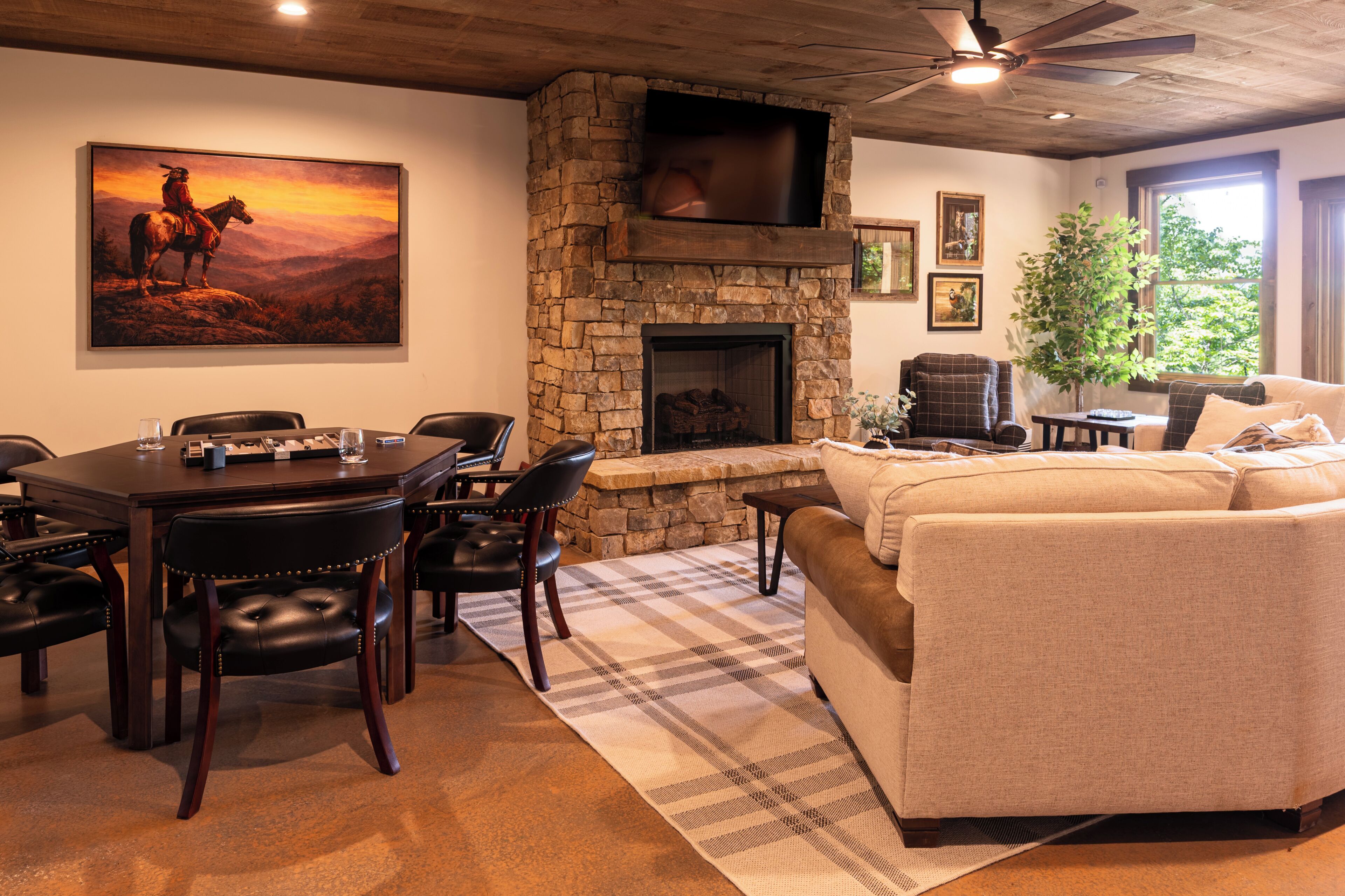 A cozy living room with a stone fireplace, a dining area with a table and chairs, a sofa, and a painting of a horse on a mountain.