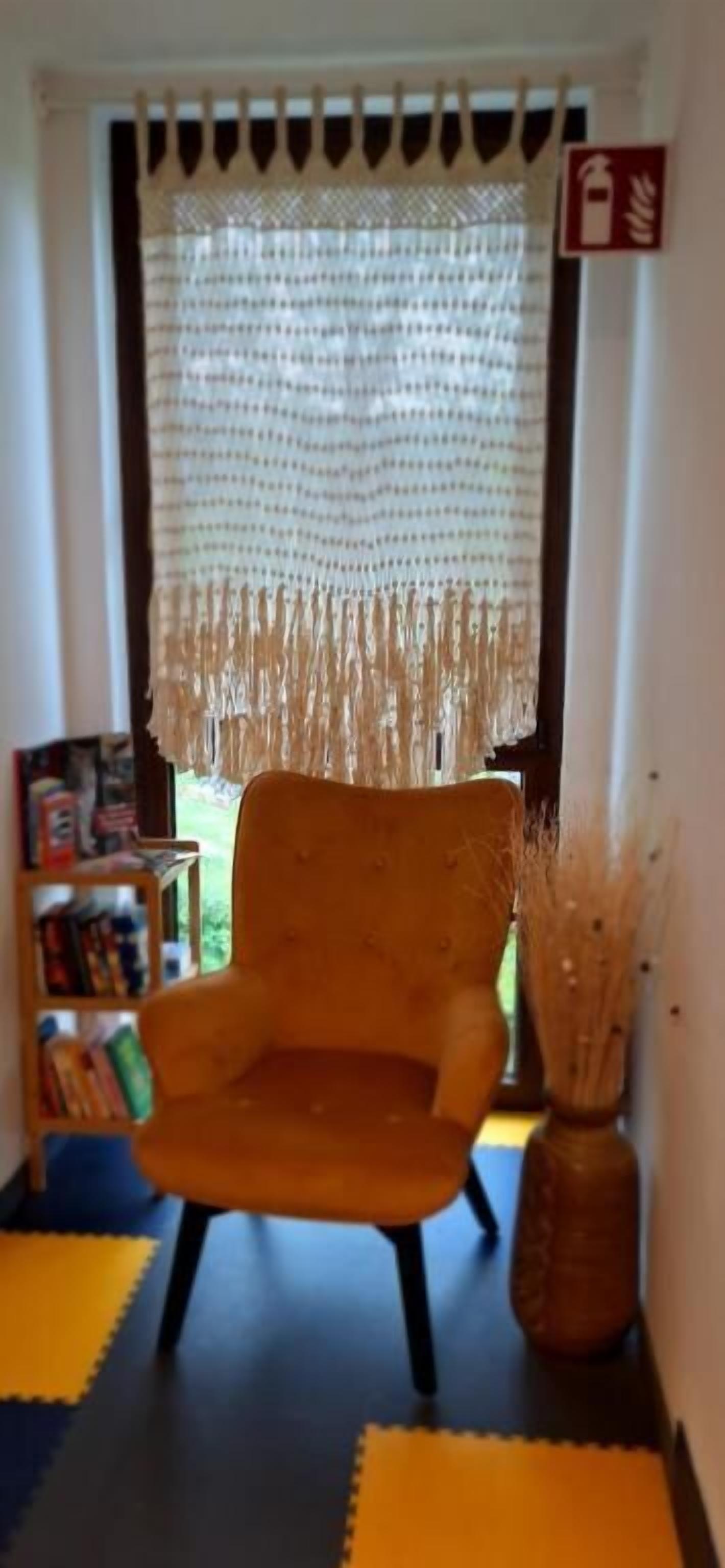 A room with a chair, a bookshelf, a decorative vase, and a curtain.