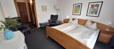 Et hotelværelse med en stor seng, et skrivebord, en stol, et lille bord og en plante.