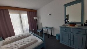 Habitación de hotel con cama, escritorio, cómoda, espejo y ventana con cortinas.