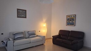 Ein Wohnzimmer mit einem weißen Sofa, einem braunen Sofa, einer Wandleuchte und zwei gerahmten Bildern.