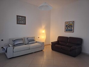 Ein Wohnzimmer mit einem weißen Sofa, einem braunen Sofa, einer Wandleuchte und zwei gerahmten Bildern.