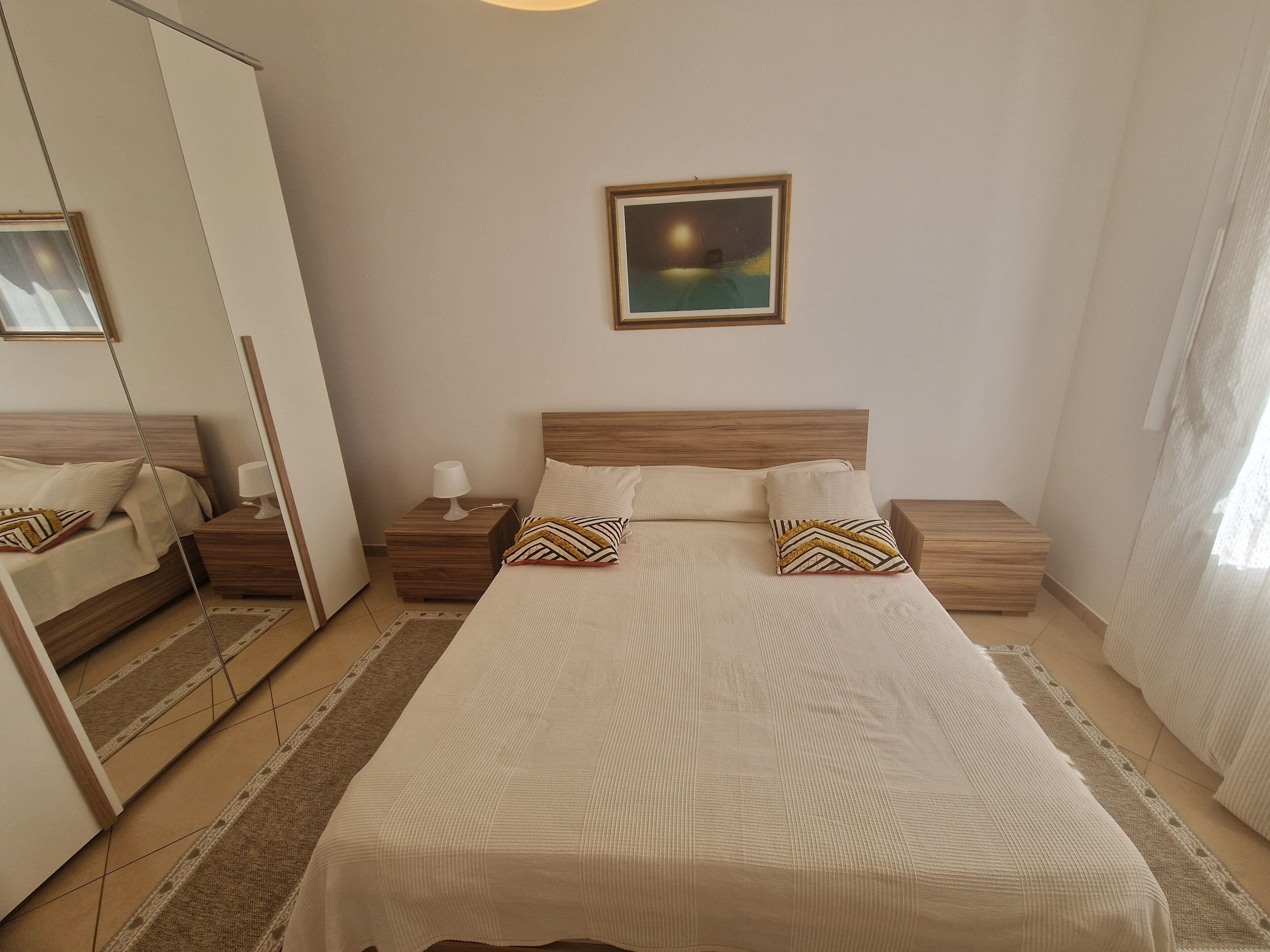 A bedroom with a large bed, two bedside tables, a nightstand, a mirror, and a framed picture on the wall.