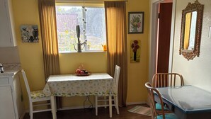 Un coin repas comprenant une table, des chaises, une fenêtre avec des rideaux, un tableau et un miroir au mur.