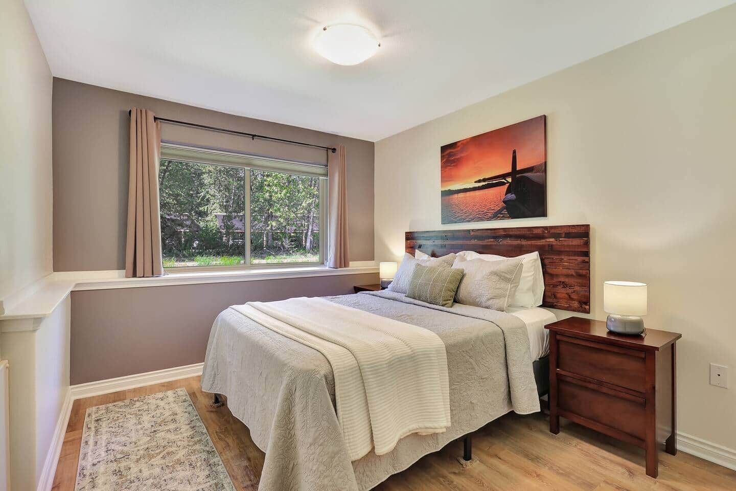 Ein Schlafzimmer mit einem Bett, einem Nachttisch, einem Fenster mit Vorhängen, einem Bild an der Wand und einem Teppich.