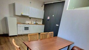 Spiseområde med et træbord og læderbænke, et køkken med hvide skabe og en mørk væg.