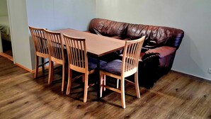 Et spiseområde med et træbord og stole, en brun lædersofa og en hvid dør.