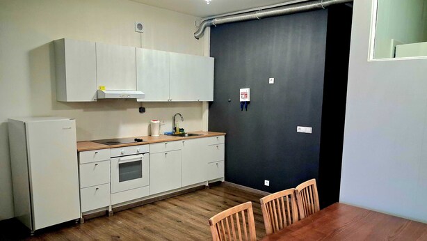 Et kompakt køkken med hvide skabe, en træbordplade, en indbygget ovn og et spisebord med stole.
