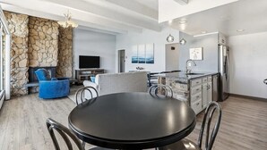 Una cocina moderna con una pared de acento de piedra, un comedor con una mesa redonda y una sala de estar con televisor y asientos.