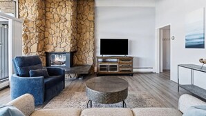 Una sala de estar moderna con una pared de acento de piedra, una chimenea, un televisor de pantalla plana y un área de descanso confortable.